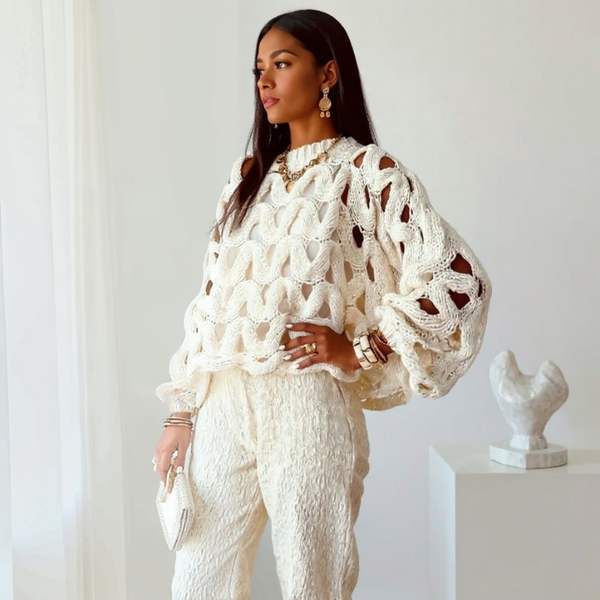 Woman wearing a white textured sweater and pants in a minimalistic setting.