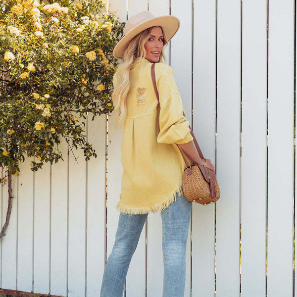 Woman in yellow dress and hat standing against a white picket fence with floral decorations.