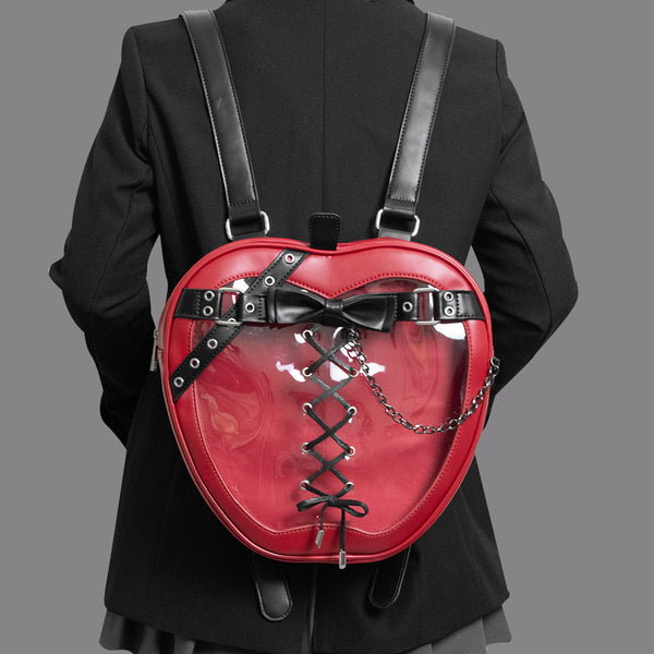 Red heart-shaped backpack with black straps and bow on a person wearing a black outfit.