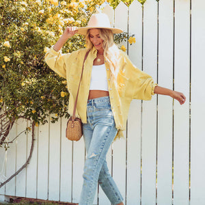Woman in yellow jacket and white hat standing in front of a white picket fence with greenery.