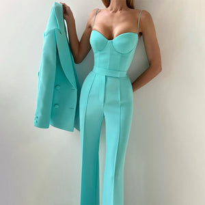 Person wearing a turquoise jumpsuit holding a matching blazer against a plain background