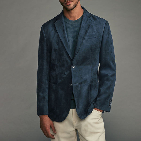 Man wearing a blue blazer over a green shirt with beige pants on a gray background