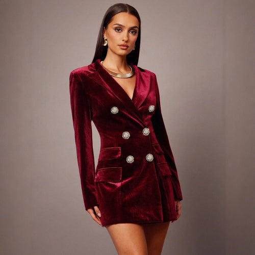 Woman wearing a burgundy velvet blazer dress with silver buttons on a gray background