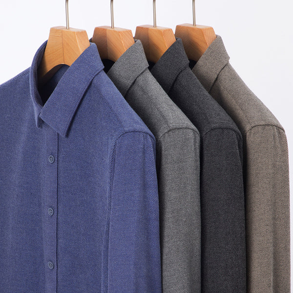 Three shirts in blue, gray, and brown hanging on wooden hangers against a white background