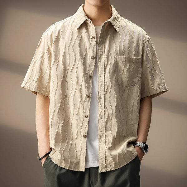 Person wearing a beige short-sleeve shirt with a subtle pattern against a neutral background