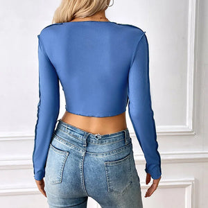 Person wearing a blue long-sleeve top and jeans against a white wall.