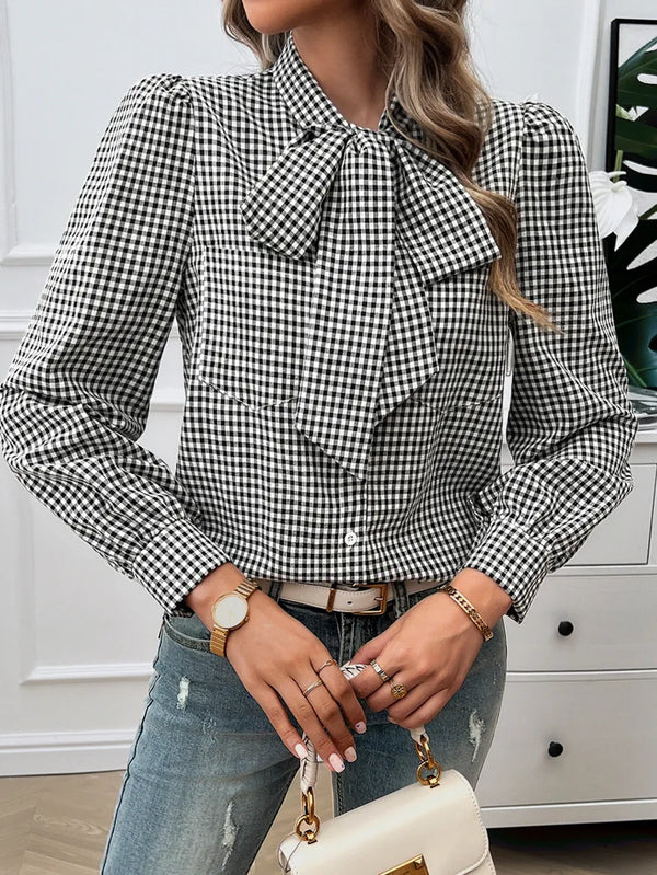 Person wearing a black and white checkered blouse with a bow tie, holding a white handbag.