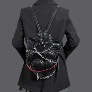 Person wearing a black leather backpack with chain details on a plain background