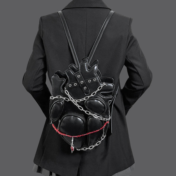 Person wearing a black leather backpack with chain details on a plain background