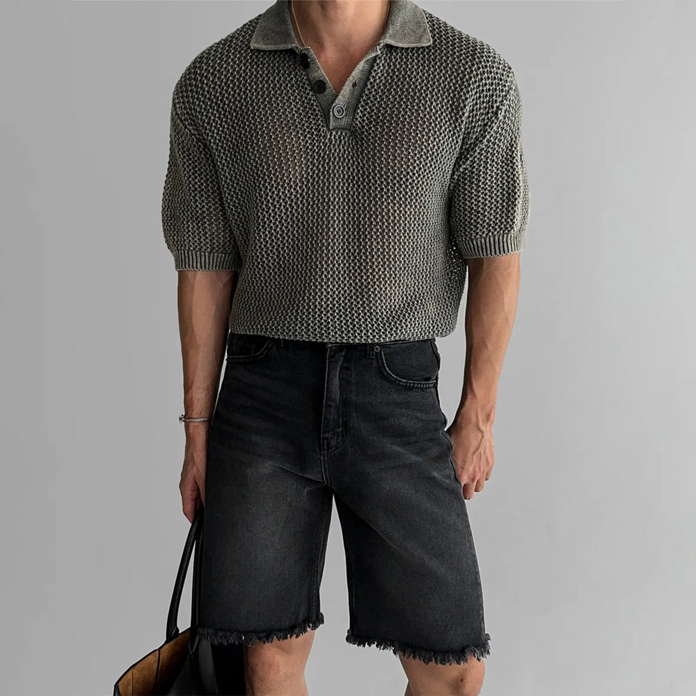 Person wearing a patterned short-sleeve shirt and black shorts on a gray background