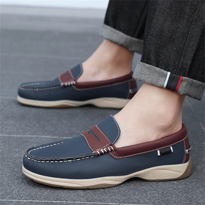 Navy loafers with brown accents worn by a person on a gray floor.