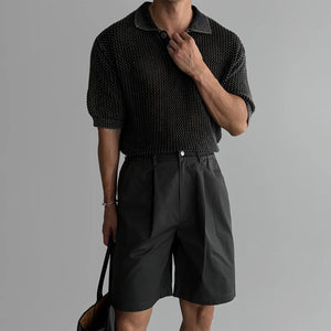 Person wearing a textured black sweater and black shorts on a gray background