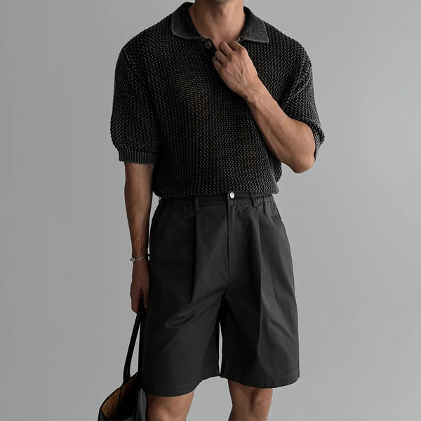 Person wearing a textured black sweater and black shorts on a gray background