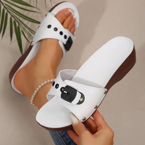 White sandals with brown soles held by a hand against a neutral background