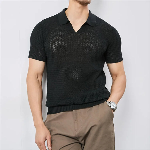 Man wearing a black short-sleeve knit polo shirt and brown pants against a light gray background