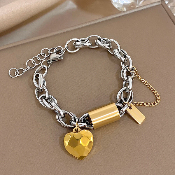 Silver chain bracelet with gold lock and heart charm on a beige surface