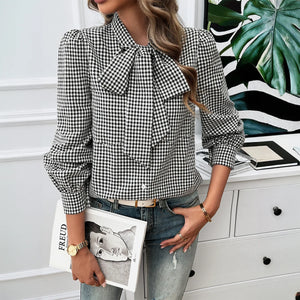 Woman wearing a black and white checkered blouse with a bow tie, holding a magazine.