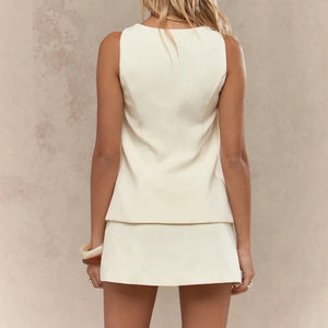 Woman wearing a cream-colored sleeveless top and skirt set against a neutral background