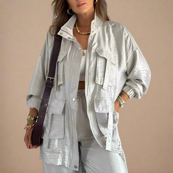 Woman wearing a light gray outfit with a jacket and pants, holding a brown bag indoors.
