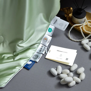 Silkworm cocoons and packaging on a gray surface with green fabric and pearls in the background.