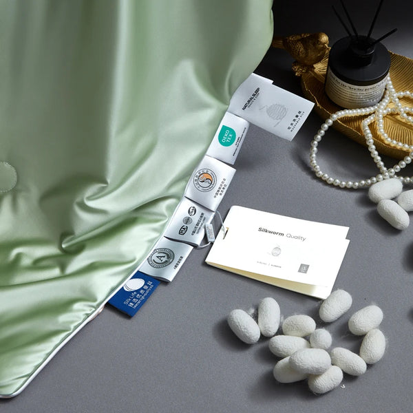 Silkworm cocoons and packaging on a gray surface with green fabric and pearls in the background.
