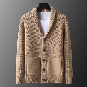 Beige knitted cardigan on a hanger against a gray background