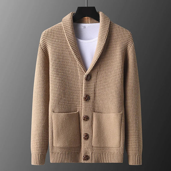 Beige knitted cardigan on a hanger against a gray background