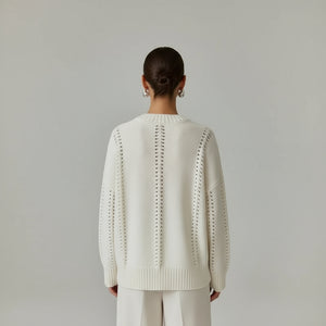 Person wearing a white sweater with intricate back design in a living room setting.