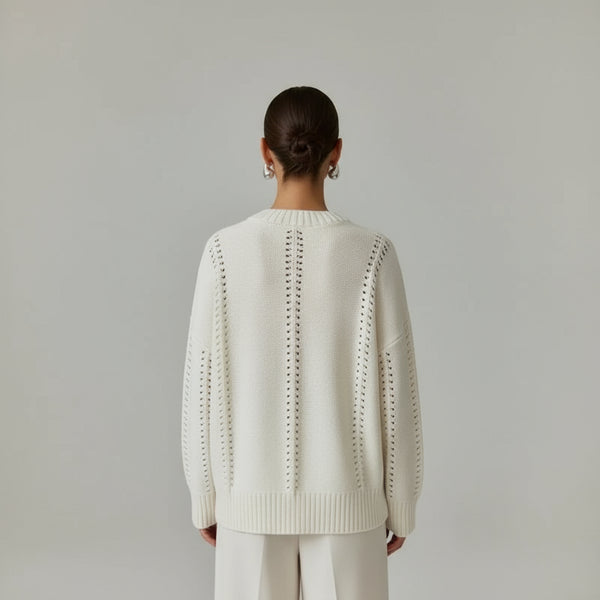 Person wearing a white sweater with intricate back design in a living room setting.