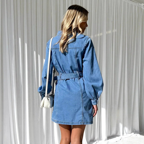 Woman wearing a blue denim dress against a white curtain background