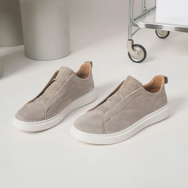 Pair of beige slip-on sneakers on a white surface with a minimal background