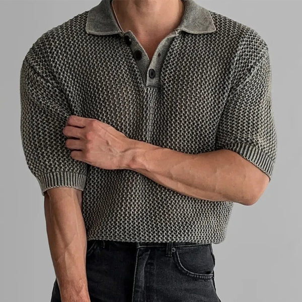 Person wearing a patterned short-sleeve shirt and black shorts holding a black bag on a gray background