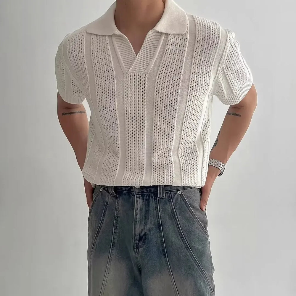 Person wearing a beige knitted vest over a white shirt with blue jeans on a plain background