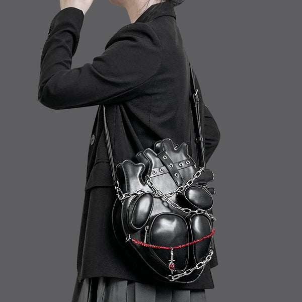 Person wearing a black coat with a unique black bag featuring chain details on a gray background