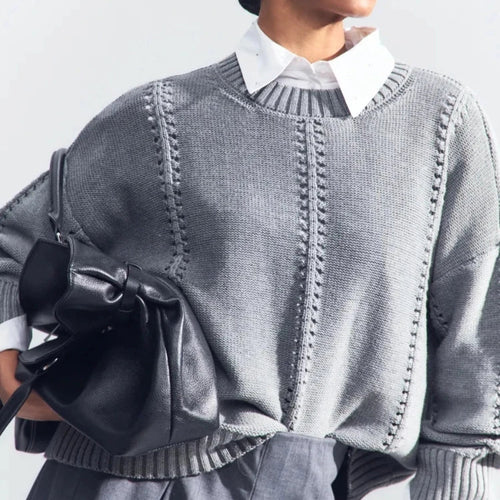 Person wearing a gray sweater with a black bag on a light gray background