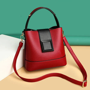 Red handbag with a black accent on a beige surface with a green background