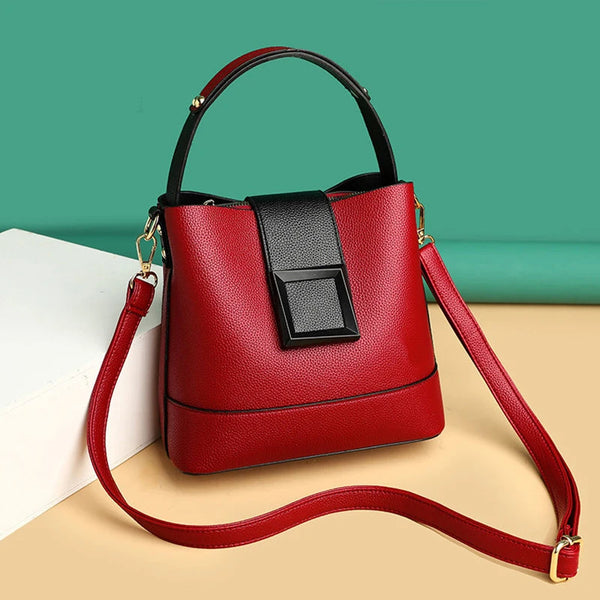 Red handbag with a black accent on a beige surface with a green background