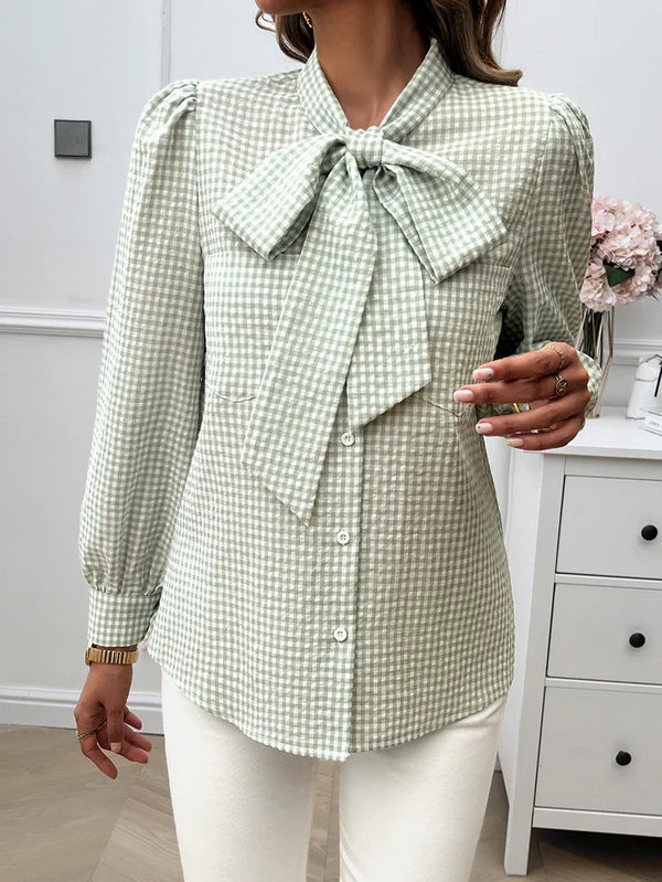 Woman wearing a green checkered blouse with a bow tie in a room.