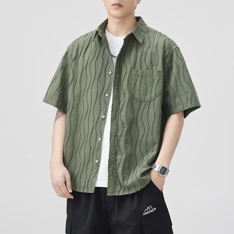 Person wearing a green patterned shirt over a white t-shirt on a light gray background
