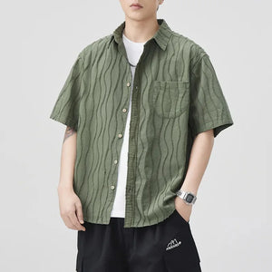 Person wearing a green patterned shirt over a white t-shirt on a light gray background