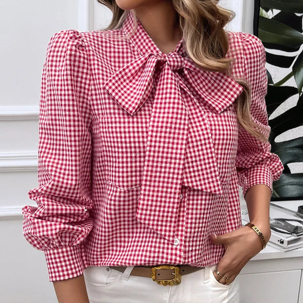 Red and white checkered blouse with a large bow worn by a person, standing against a neutral background.