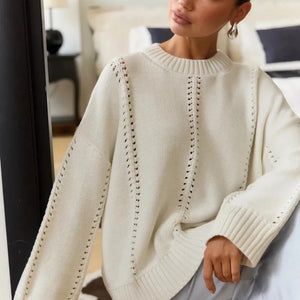Person wearing a cream-colored sweater with intricate patterns in a blurred indoor setting