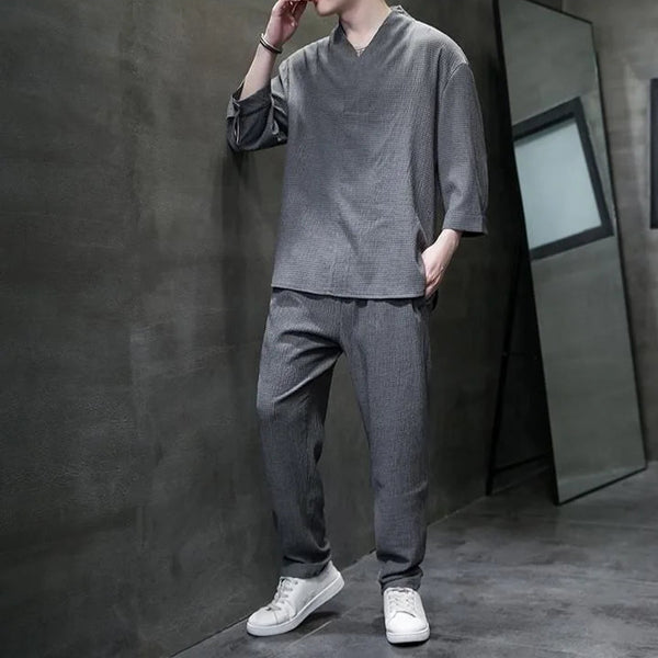 Person wearing a gray outfit with white sneakers against a dark wall.