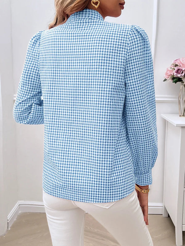 Person wearing a blue checkered shirt in a room with a white wall and a small table with flowers.