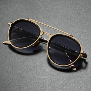 Gold-framed sunglasses with dark lenses on a gray background