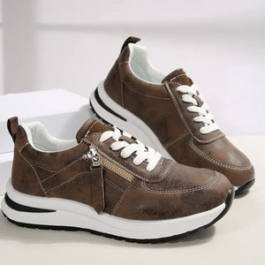 Pair of brown sneakers with white laces on a light background