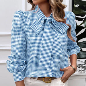 Woman wearing a blue and white checkered blouse with a bow tie in an indoor setting.