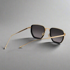 Gold-framed sunglasses with black lenses on a light gray background