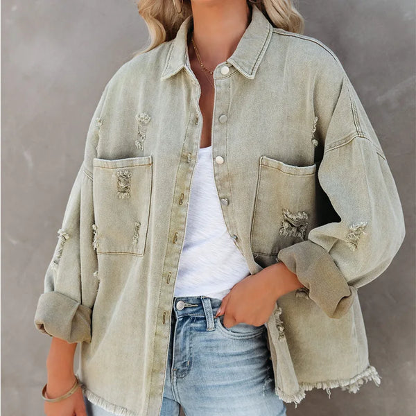 Person wearing a light green denim jacket over a white shirt and blue jeans against a gray background