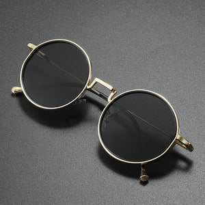 Round sunglasses with gold frame and black lenses on a gray background